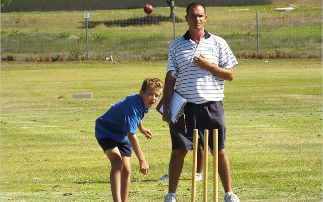 Leon Wessels van Laerskool Gansbaai boul terwyl die afrigter van Die Bron, Graham Stieger toekyk.